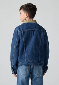 Τζάκετ τζιν σε σκούρο μπλε, με γιακά από κοτλέ. Συνδυάζεται με ανοιχτό μπλε τζιν, εμφανίζοντας πλάγιες όψεις και λεπτομερή ραφή στις τσέπες.