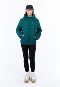 Teal gewatteerde pufferjack met capuchon, frontale rits en zijzakken; gecombineerd met zwarte broeken en crèmekleurige met pels gevoerde laarzen.