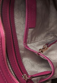 Interno di una borsa a tracolla in pelle rosa con una trama liscia, caratterizzato da una fodera chiara con un motivo a logo, molteplici scomparti e una cerniera dorata.