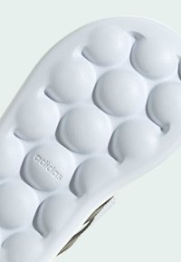 Suela de zapato de goma blanca con un patrón de burbujas texturizadas y el logotipo en relieve "adidas", con un borde gris que acentúa el diseño.