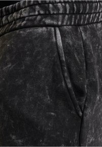 Svarta joggers med ett strukturerat tyg som har ett slitet mönster. Elastisk midja och sidofickor är synliga.