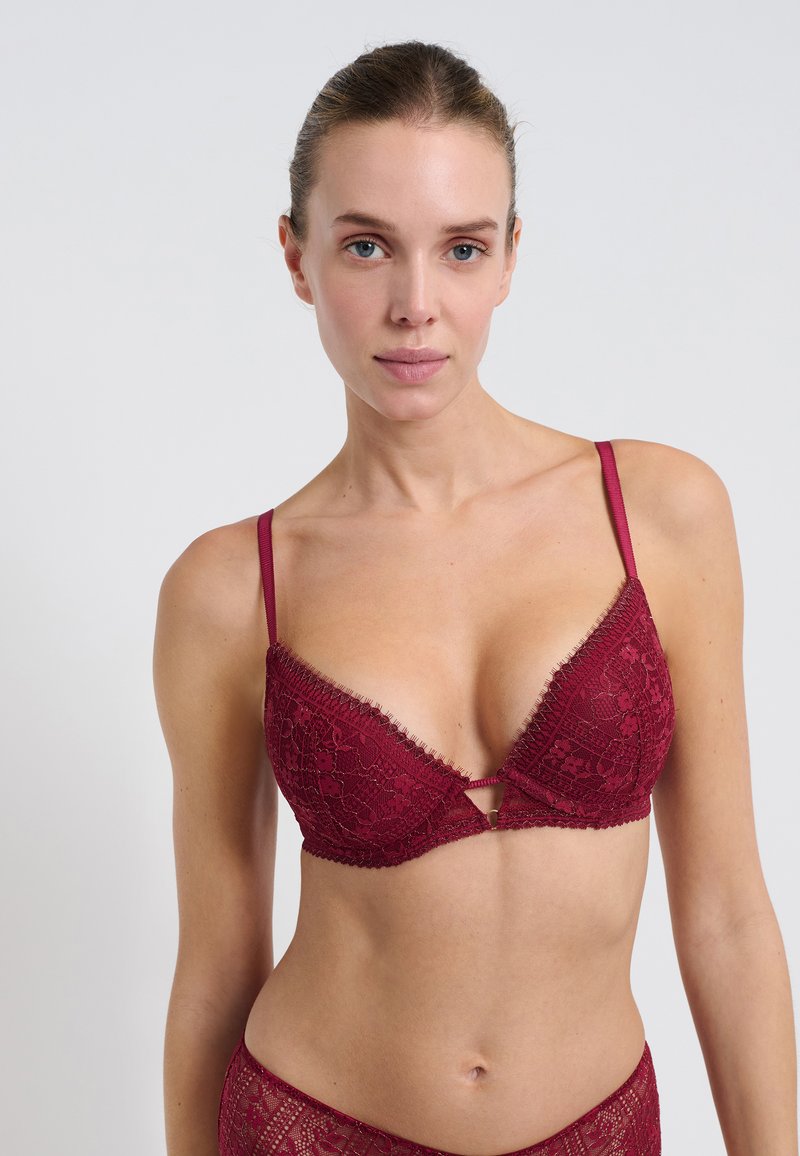 Bralette in pizzo bordeaux con scollatura profonda, sottili spalline regolabili e cuciture decorative lungo i bordi. Dettaglio a chiave sul davanti.