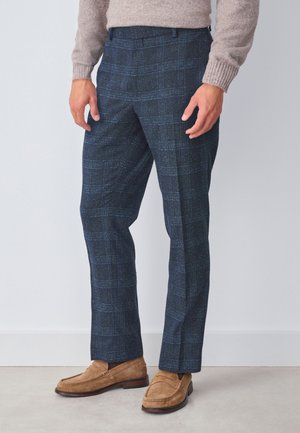 Pantaloni a quadri navy in tessuto strutturato con accenti verdi, con taglio dritto e tasche laterali, abbinati a mocassini marroni.