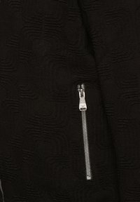 Schwarzer strukturierter Stoff mit einem wellenförmigen Muster; verfügt über einen silbernen Reißverschluss an der Seite, der dem Design ein funktionales Detail verleiht.