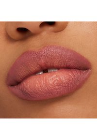 Des lèvres mauves mates avec une texture douce, montrant des lignes subtiles et une apparence naturelle, positionnées contre un teint de peau lisse.