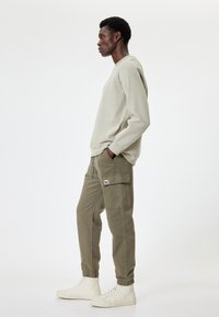 Lichtgrijze sweatshirt met ribbelstructuur, gecombineerd met olijfgroene cargo broeken met zijzakken. Outfit compleet met witte hoge sneakers.