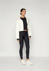 Izrezani bijeli kaput od umjetnog krzna preko crne majice dugih rukava, uparen s crnim tajicama i bijelim sportskim cipelama.