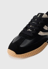 Baskets noires avec des panneaux en daim et en cuir, accents en motif serpent texturé, lacets ronds et semelle en caoutchouc gomme avec une texture à petits points.
