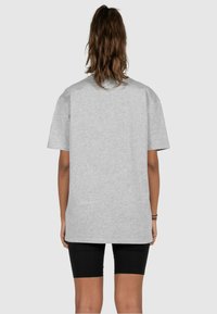 Gray cotton oversized t-shirt with short sleeves, featuring a round neckline and raw hem, paired with black fitted shorts.