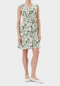 Ärmelloses Wickelkleid mit Blumenmuster aus leichtem Stoff, das ein grün-lila Muster auf weißem Hintergrund zeigt, mit einer taillierten Taille und einem ausgestellten Rock.
