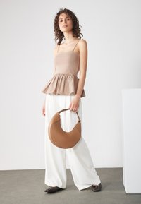 Beige peplum topp med tynne stropper, hvite vide bukser og brun halvmåneformet håndveske. Teksturert stoff og glatte hardware-detaler.