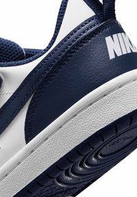 Κοντινή λήψη της φτέρνας ενός ναυτικού μπλε και λευκού αθλητικού παπουτσιού Nike που δείχνει την υφή της σόλας, το ράψιμο από δέρμα και μέρος του λογότυπου της Nike.