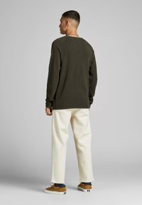 Olijfgroen gebreid sweater met lange mouwen en een relaxte pasvorm, gecombineerd met crèmekleurige rechtlopende broeken en bruine sneakers.