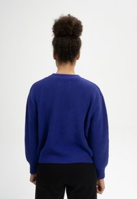 Blau gestrickter Pullover mit langen Ärmeln, lockerer Passform und Rundhalsausschnitt. Strukturierter Strick, Saum endet auf Hüfthöhe.
