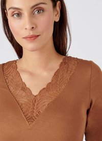 Top marrone con scollatura a V e dettagli in pizzo intricati. Il tessuto ha una texture liscia e una vestibilità aderente, esaltando il design.