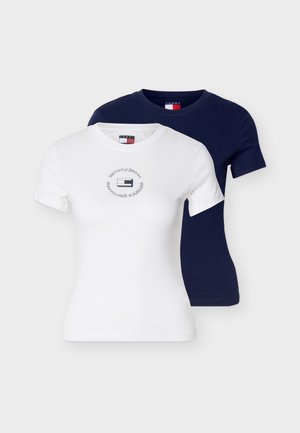 Dos camisetas de manga corta con cuello redondo, una blanca con un logo circular y otra azul marino lisa, exhibidas sobre un fondo liso.