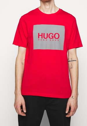 Rotes Baumwoll-T-Shirt mit einem grauen rechteckigen Grafikdesign, das den Text "HUGO" und "HUGO BOSS" zeigt, kurzem Ärmel und klassischer Passform.