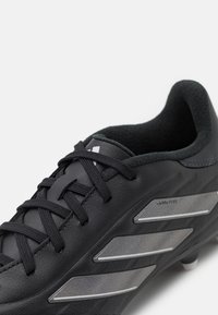 Scarpa da calcio nera con tomaia in pelle texturizzata, dotata di tre strisce metalliche argentate sul lato e lacci neri. Morbida imbottitura alla caviglia.