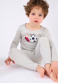 Pigiama in cotone grigio con una stampa divertente di calcio, caratterizzato da una scarpa rossa e un pallone. Il design include il testo “Gol!” in nero.