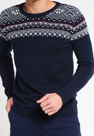 Marineblauwe crew-neck trui met een wit en kastanjebruin geometrisch breipatroon over de schouderpartij. Geribbelde manchetten en zoom, gemaakt van een zacht, wolachtig materiaal.