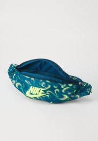Sac banane Nike avec un motif tourbillonnant bleu et vert, doté d'une fermeture éclair et d'une poche intérieure en mesh. Logo imprimé en jaune fluo.