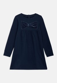 Abito lungo a maniche, di colore azul navy, con un fiocco di velluto testurizzato sul petto, vita arricciata e scollatura rotonda. Chiusura con bottoni sul retro.