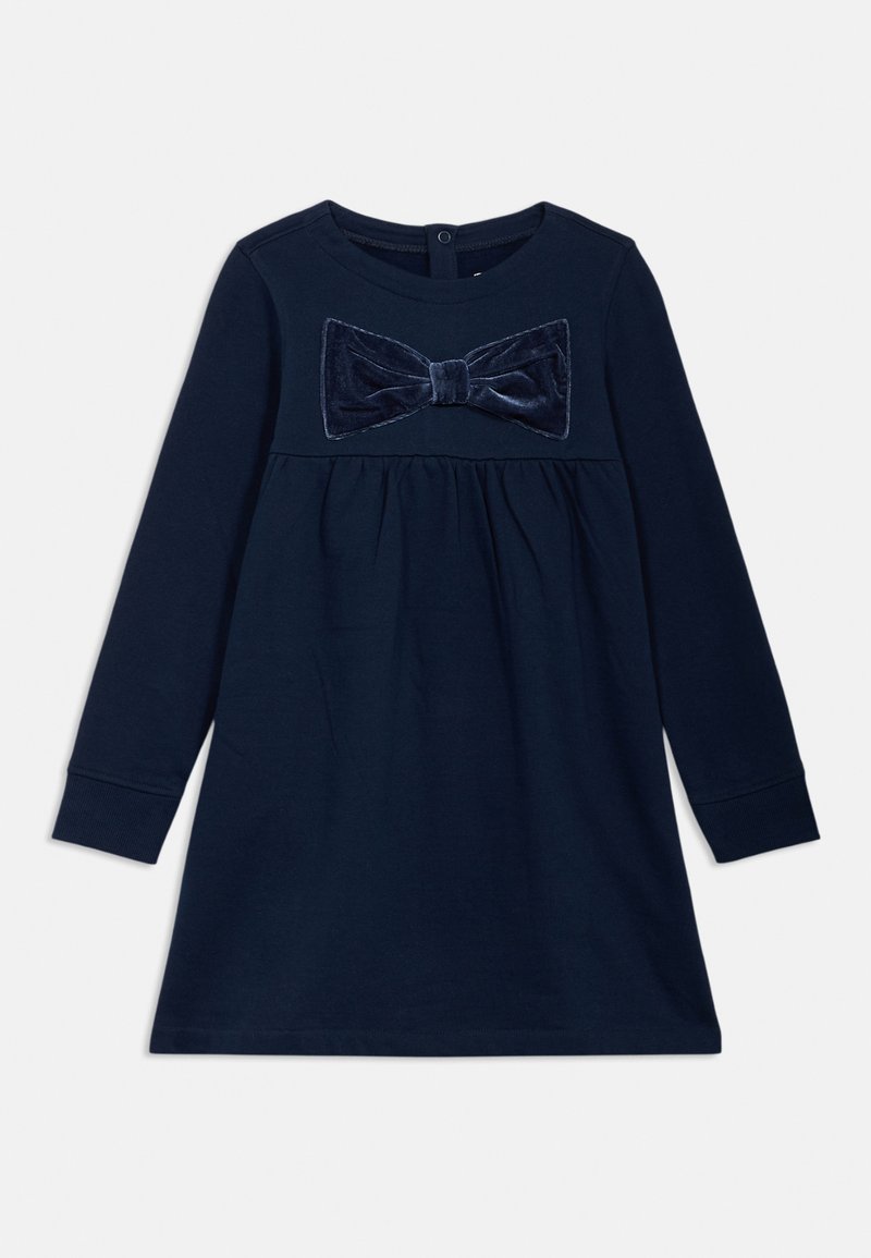 Abito lungo a maniche, di colore azul navy, con un fiocco di velluto testurizzato sul petto, vita arricciata e scollatura rotonda. Chiusura con bottoni sul retro.