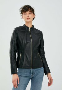 Giacca di pelle nera con colletto rialzato, chiusura con zip dorata e due tasche laterali con zip; finitura texturizzata e design attillato.