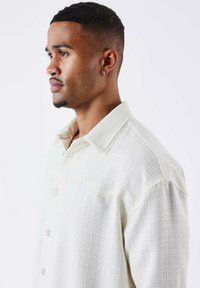 Licht crèmekleurig geweven shirt met een kraag, knoopsluiting aan de voorkant en gestructureerde stof. Kenmerkt zich door een subtiel ruitpatroon en een relaxte pasvorm.