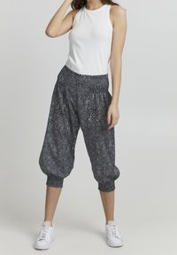 Svarta mönstrade harembyxor med resårmidja och avsmalnande muddar, ihop med en vit ärmlös topp och vita sneakers.