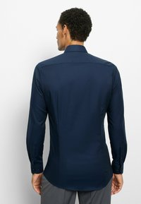 Marineblaues langärmliges Hemd mit strukturiertem Kragen, strukturiertem Stoff und knöpfbaren Manschetten. Maßgeschneiderte Passform, glatte Oberfläche und Rückenpasse als Detail.