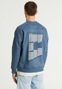 Felpa blu con un design testurizzato sulla schiena che presenta un motivo a griglia. Tessuto morbido, scollatura rotonda e polsini a costine.