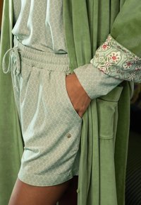 Hellgrünes Loungewear-Set mit einem gemusterten Shorts und Oberteil. Der Bademantel ist weich, in einheitlichem Grün, mit detaillierten floralen Akzenten an den Ärmeln.