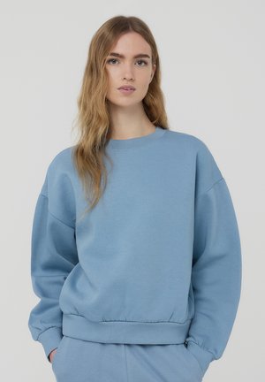 Felpa azzurra chiara in morbido cotone felpato, con collo a giro, spalle scese e polsini e orlo a costine per un fit rilassato.