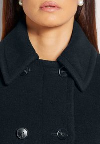 Black wool coat featuring a notched collar, two black buttons, and a soft texture. The focus is on the collar and buttons.
