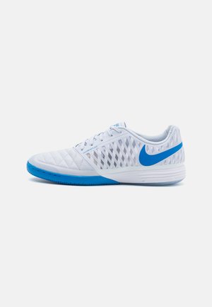 White athletic shoe with blue accents, featuring a quilted design and mesh side panels for ventilation. Rounded toe and rubber sole.