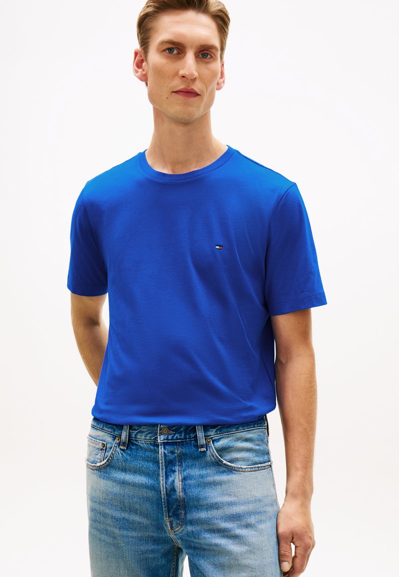 Μπλε βαμβακερό μπλουζάκι, με στρογγυλή λαιμόκοψη και κοντά μανίκια. Μικρή λεπτομέρεια λογότυπου στο στήθος. Συνδυάζεται με τζιν παντελόνια με ανοιχτό χρώμα.