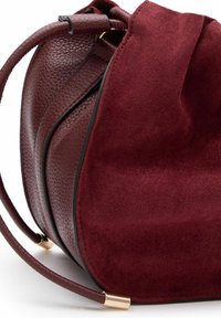 Borsa bordeaux realizzata in pelle texturizzata e suede, con una forma arrotondata, rifiniture nere a contrasto e accessori in metallo dorato.