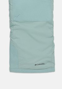 Lys blå Columbia-bukser med en jevn tekstur, som har en sidelomme og en logo på kanten. Enkel design, skreddersydd snitt.