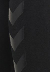 Zbliżenie czarnej tkaniny z trzema ciemnoszarymi skośnymi paskami chevron po lewej stronie.