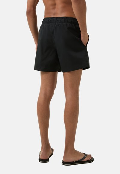 Shorts de bain noirs avec une taille élastique et des poches latérales, dotés d'une texture lisse et d'une longueur au-dessus du genou. Design uni.