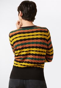 Gestreifter Strickpullover mit wellenförmigen Mustern in Gelb, Orange, Grün und Schwarz; gerippter schwarzer Saum; strukturierter Stoff.