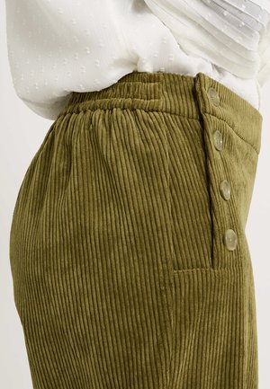Pantalones de pana verde oliva con costillas verticales, cinturilla elástica y tres botones decorativos en la parte frontal. Se visible un bolsillo lateral.