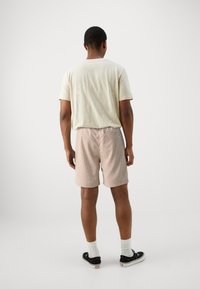 Camiseta beige claro combinada con pantalones cortos a cuadros en tonos suaves de durazno y rojo. El modelo lleva calcetines blancos y zapatillas negras.