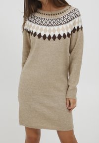 Robe-pull beige en maille avec manches longues et un motif géométrique de losanges marron et blancs autour du col et des épaules.