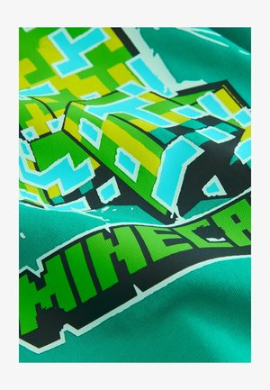 Zelené grafické tričko s pixelovým blokovým dizajnom v žltej a modrej farbe, s nápisom "MINECRAFT" tučným čiernym a jasne zeleným písmom.