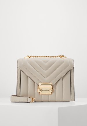 Beige doorgestikte leren handtas met een gouden kettinghandvat en een rechthoekige gouden sluiting met de gravure "MICHAEL KORS", geplaatst op een witte ondergrond.