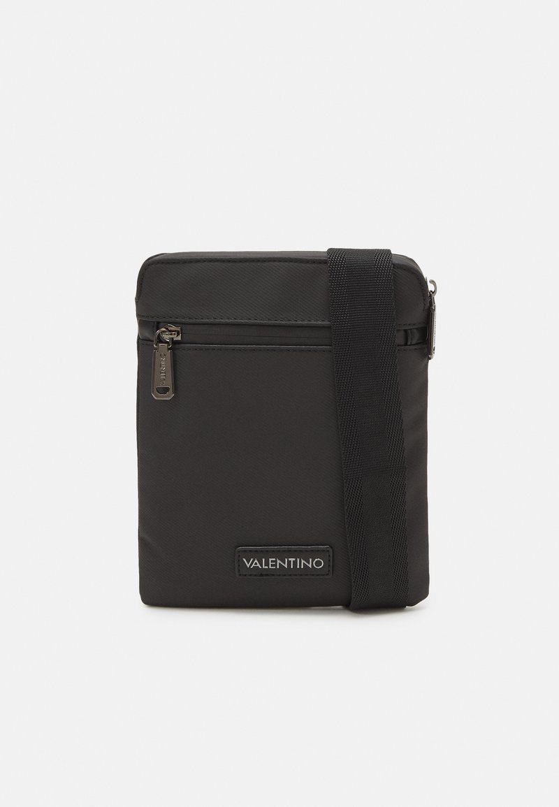 Borsa a tracolla nera in nylon con scomparto principale con zip, tracolla regolabile e un patch con logo sulla parte anteriore. Design rettangolare semplice.