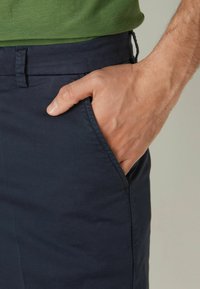 Navy tygbyxor med en slät textur, med en sidficka och en avslappnad passform, bärs med en grön skjorta.