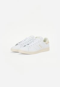 Sapatilhas brancas com um cabedal de couro liso, com detalhes perfurados, atacadores planos e uma sola texturizada em off-white. Detalhes em dourado nas laterais.